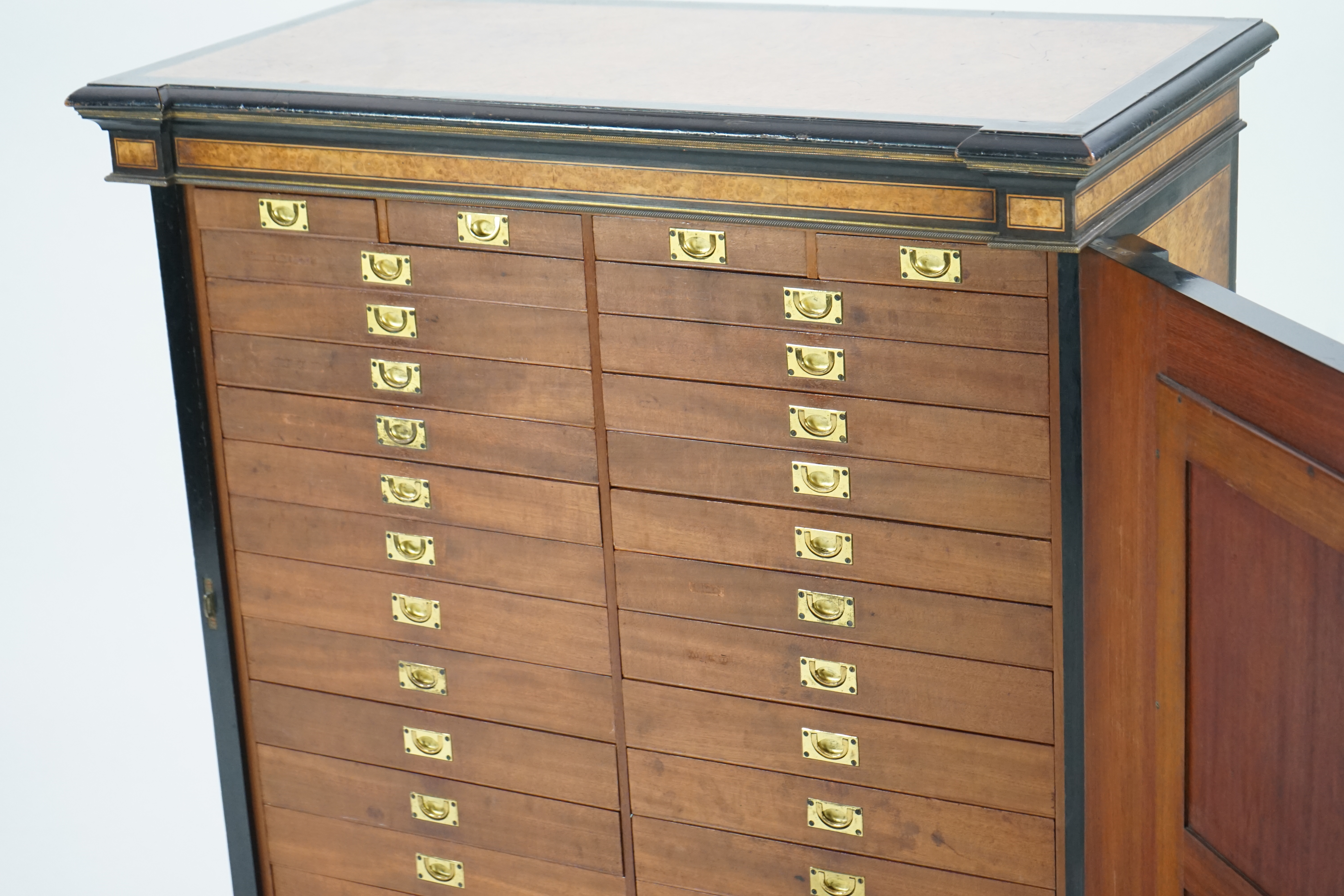 A Victorian ebony banded amboyna wood collector's cabinet, by Holland & Sons, with inverted breakfront top and single mirrored door enclosing four frieze and two banks of thirteen graduated drawers fitted with recessed b